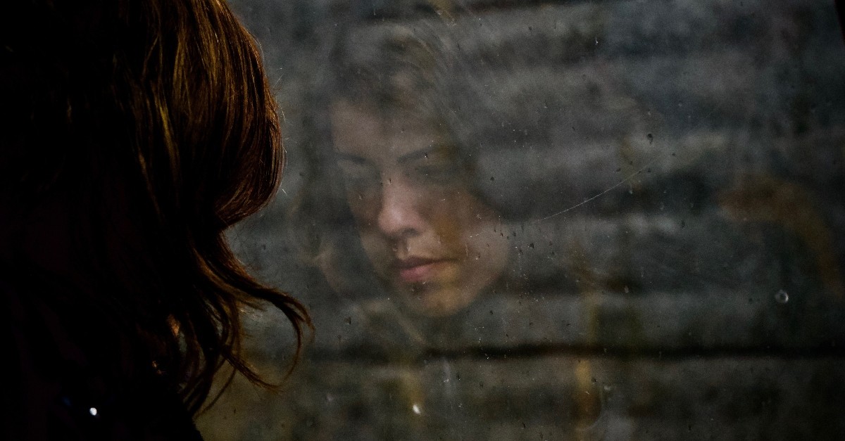 sad woman's reflection looking out of window with raindrops